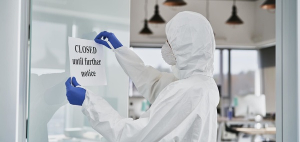 A man wearing a lab suit holding a paper with a 'closed until further notice' written on it