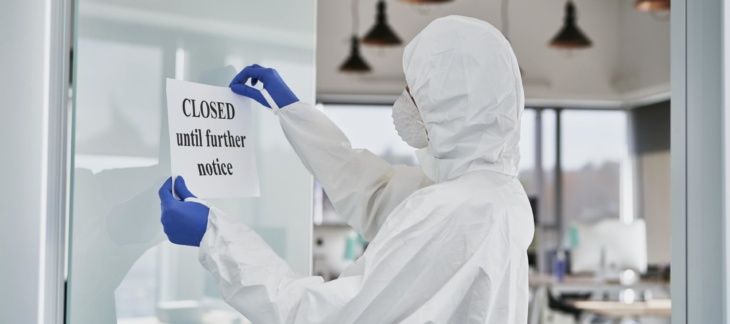 A man wearing a lab suit holding a paper with a 'closed until further notice' written on it