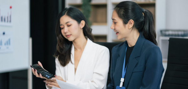 Two female finance professionals reviewing monthly bookkeeping records and calculating figures to ensure accuracy