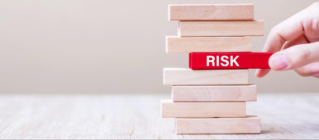 Hand removing a red block labelled Risk from a stacked wooden tower, representing tax audit risk reduction