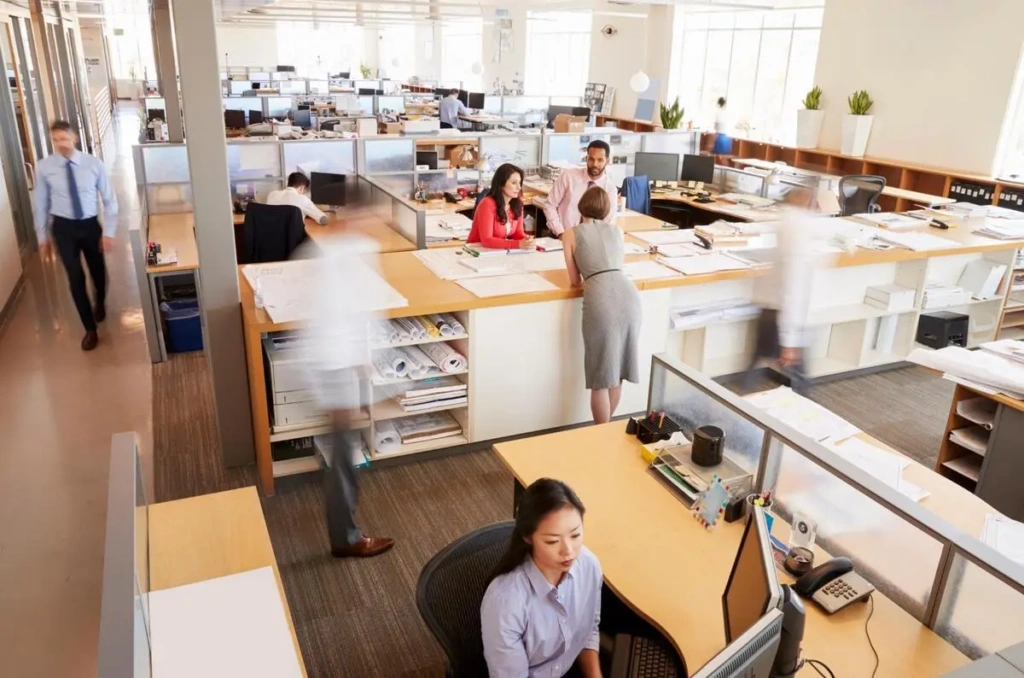 Busy open-plan office with employees working at desks and walking between cubicles
