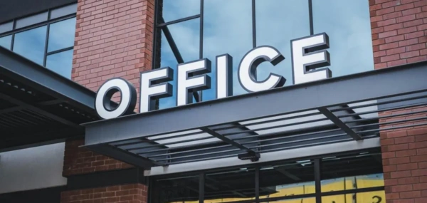 Illuminated OFFICE signage mounted above the entrance of a modern brick and glass commercial building