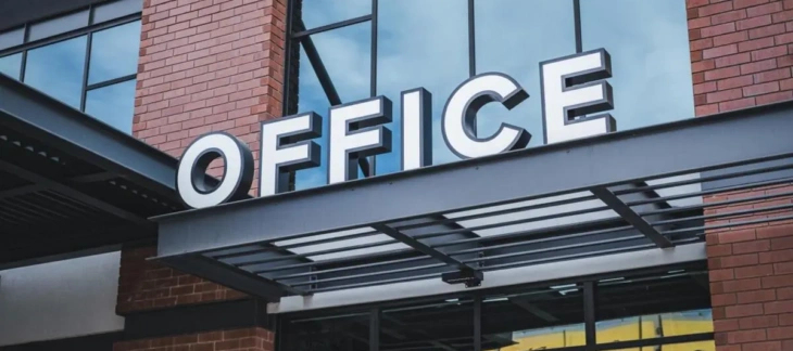 Illuminated OFFICE signage mounted above the entrance of a modern brick and glass commercial building